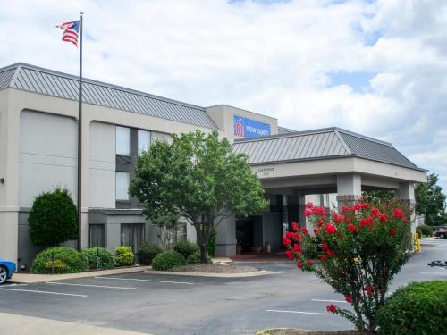 The Motel 6 in Conway, Arkansas has a flag pole and red flowers in the beds in the parking lot. The building is offwhite with a covered loading dock.