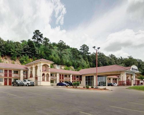 The Quality Inn in Conway, Arkansas backs up to a cliff covered in greenery. The inn has a red roof and red railings on the balconies. There is a large parking lot in front.