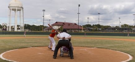 A boy standing at home base holding a bat and the catcher and umpire behind him looking out at the field at Conway Station Park in Conway, Arkansas