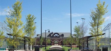A faraway view of the building at City of Colleges Park in Conway, Arkansas. A center walkway in front of the brown brick building stretches between two baseball fields.