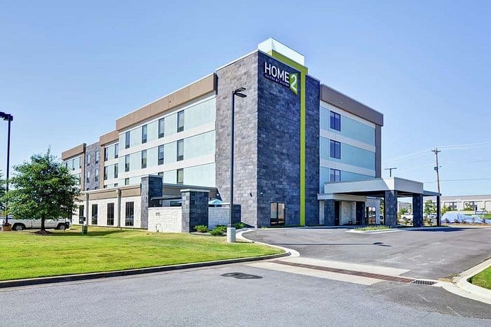 Home 2 Suites in Conway, Arkansas. A modern looking building with gray stone sides and blue paneling for each floor.