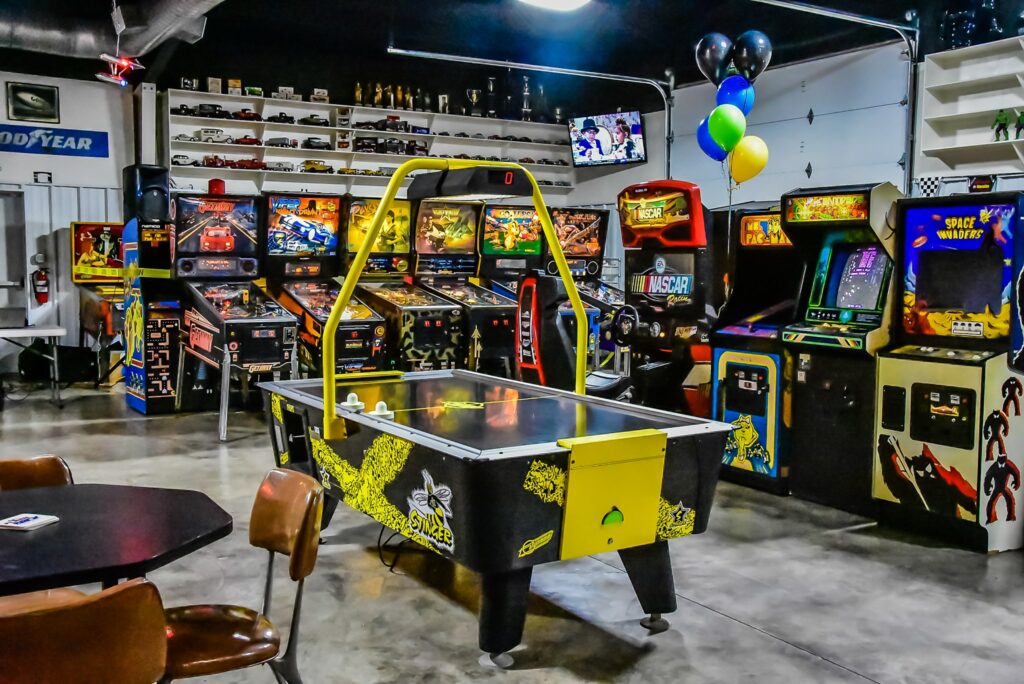 There is a wall of pinball and arcade games and a black and yellow air hockey game stands in front of them at Flashback Pinball Arcade in Conway, Arkansas.