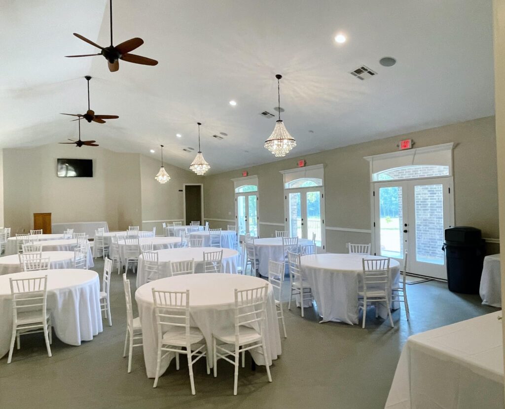A large event room set with circle tables covered in white tablecloths with five white chairs at each table at the Cypress Manor Event Center in Conway, Arkansas.