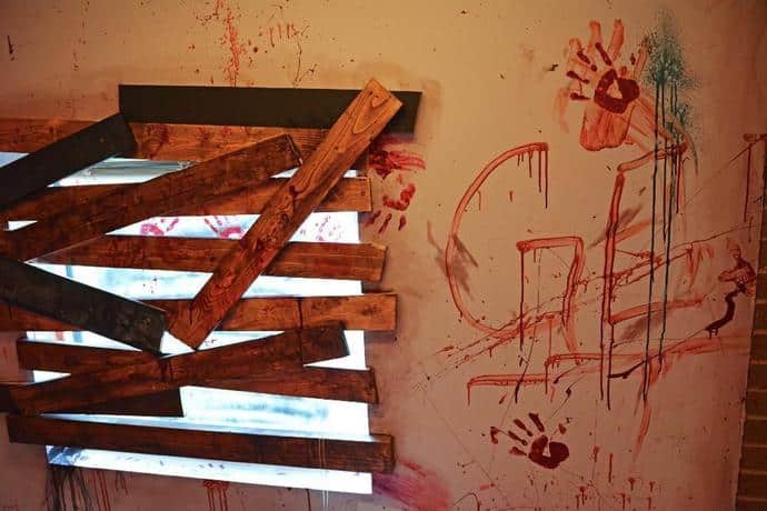 A boarded up window is broken and the dingy wall next to it is smeared with bloody handprints and the word "GET" at Ozark Escape Conway in Conway, Arkansas.