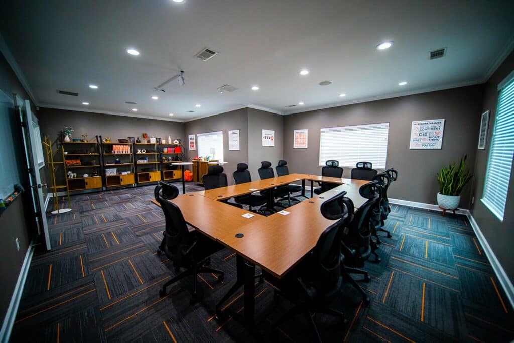 A meeting room with blue blocked carpet and narrow orange stripes at the Conway Conference Center in Conway, Arkansas. The walls are hung with inspirational posters and wooden conference tables are arranged in the center of the room with large black office chairs surrounding it.