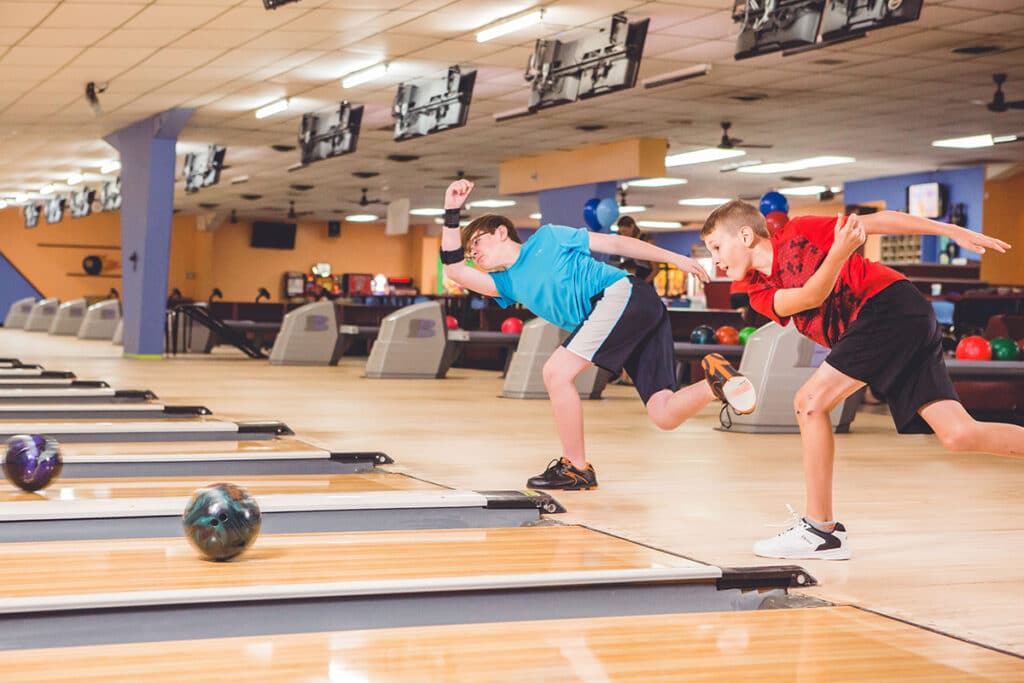 Two preteen boys throw bowling balls down the lane. Both boys are standing on one leg with an arm bent across their body. One boy is wearing a bright blue shirt and the other is in red at Conway Family Bowl in Conway, Arkansas.