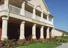 A building with white pillars and a second floor porch railing called the Centennial Valley Country Club Event Center in Conway, Arkansas. The front has two small green gardens split by a sidewalk.