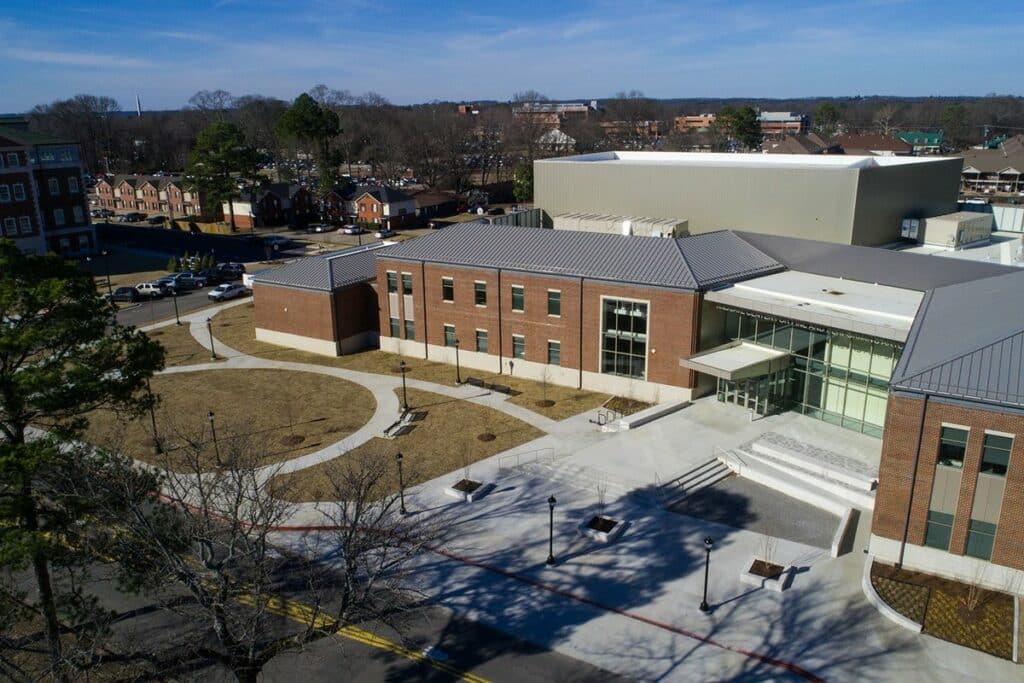 A brick classroom building called Windgate Center for Fine and Performing Arts with a glass window front panel and a white concrete patio at UCA in Conway, Arkansas.