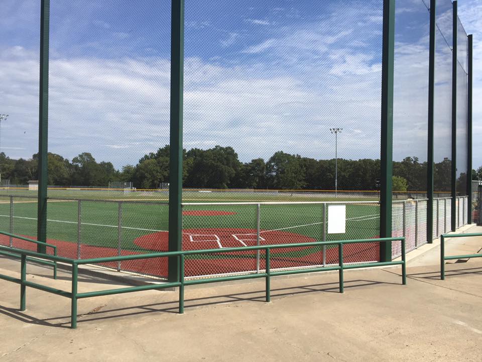 A look at a well-manicured baseball field at Don Owens Sports Complex in Conway, Arkansas through a net behind green railings.